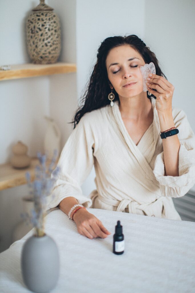 Woman giving herself a  Gua Sha facial massage https://karlacorral.com/wp-content/uploads/2023/04/pexels-elina-fairytale-3865665-683x1024.jpg