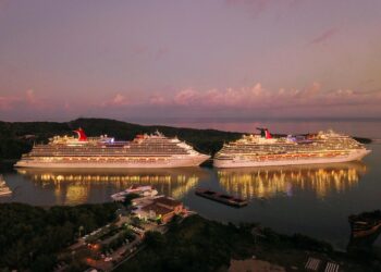 Two illuminated cruise ships docked at Coxen Hole, Honduras during twilight.