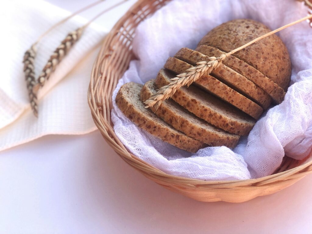 Sliced whole wheat bread in a woven basket, garnished with wheat stalks for a rustic food presentation.